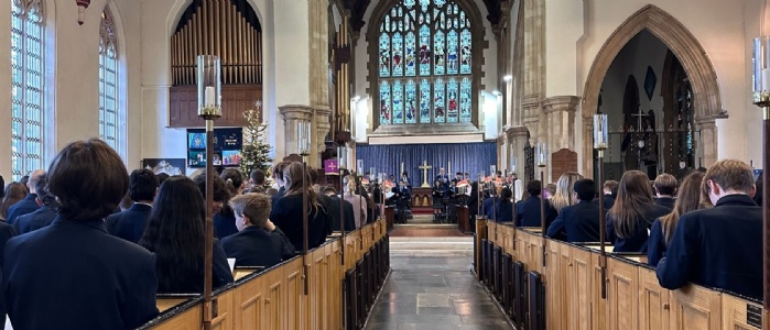 Church pews filled with students looking to the alter and beautiful stained glass window with the choir of 30 students and staff looking back at them